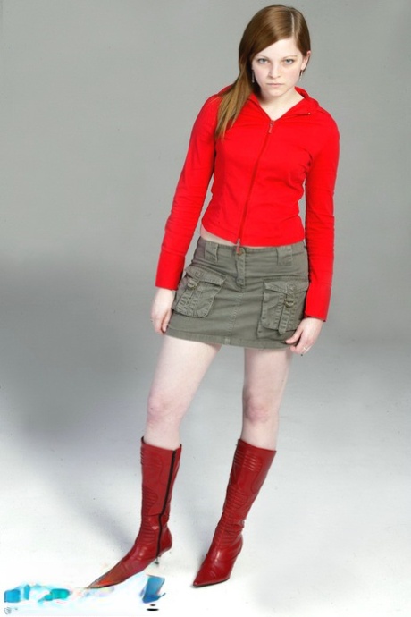 A pale redhead named Lilly slowly switches between a pair of red leather boots and a black G-string.