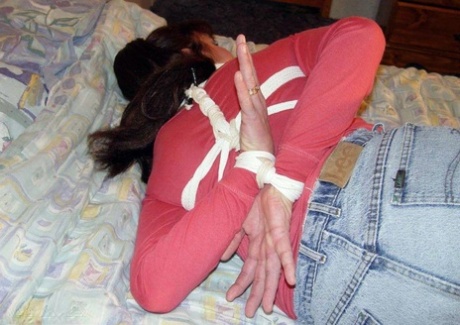 In her clothes, a white girl is left tied up and pinned down on a bed.