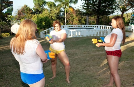 A group of girls with big t-shirts and white t-shirts are used as water guns in a yard with super-soaker construction to soak up the sun's ultraviolet radiation.