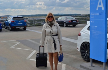 The airport sees a mature blonde woman wearing a trench coat.