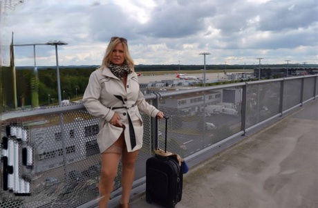 An airport waitress wears a trench coat and exposes her blonde locks.