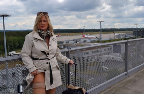 Young blonde wears revealing trench coat while waiting at the airport.