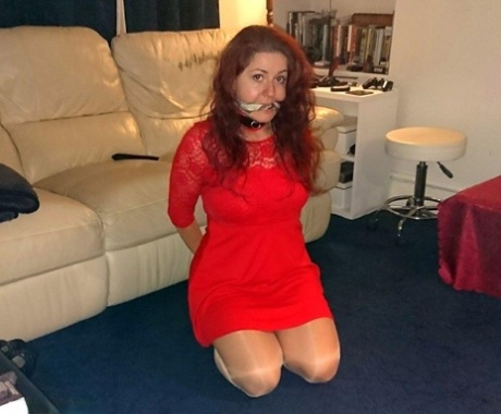 A red-headed woman is seen wearing a collar and leash in a few outfits while being gagged.
