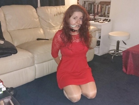 A red-headed woman is seen wearing a collar and leash in a few outfits while being gagged.