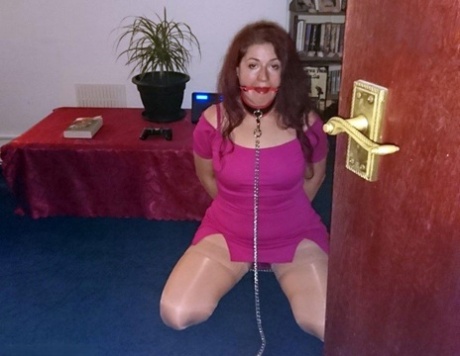 While wearing a collar and leash in various outfits, the red-headed female is gagged.