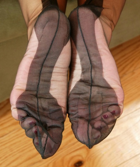 An Asian model seizes one of her fully robed nylons while sitting on a couch.