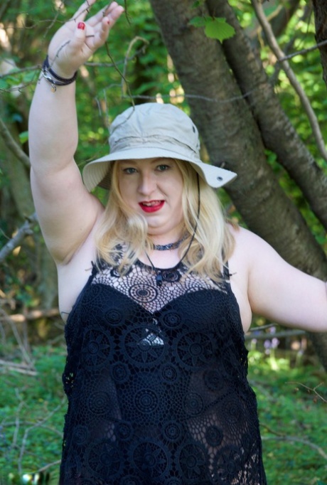 Blonde woman who is overweight exposes herself naked by a tree while wearing a sun hat.