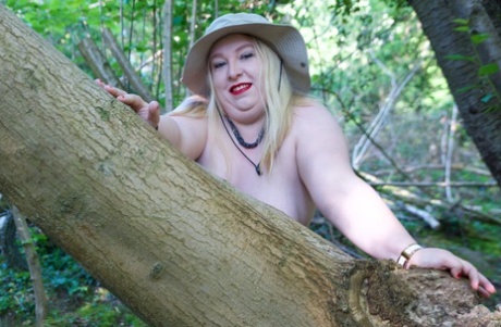 Blonde with excess weight is bared in front of an unidentified tree while wearing sunglasses and a sun block.