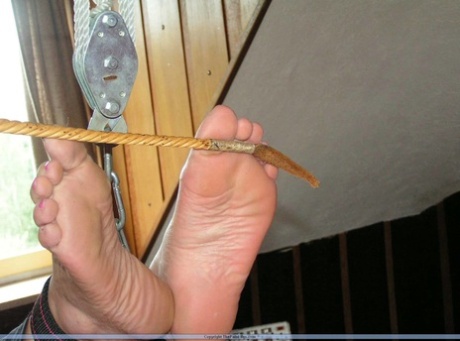 Prior to caning her bare feet, the older blonde has her saggy tits tightly grasped.