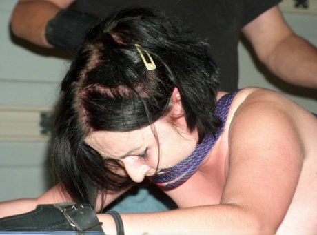 In bondage, a dark haired girl has her buttocks covered in hot wax while being pulled back into the braces.