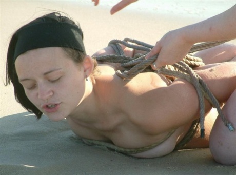 A naked girl is tied up with rope by her lesbian partner as the waves arrive.