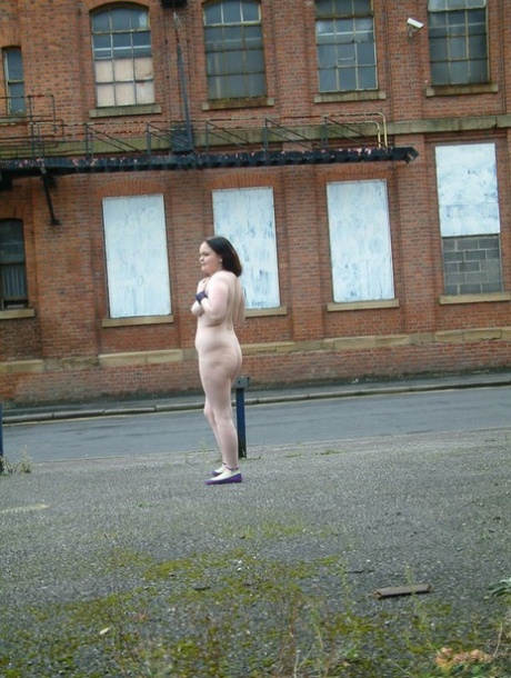 Naked walk: A plump girl walks through an industrial area's parking lot.