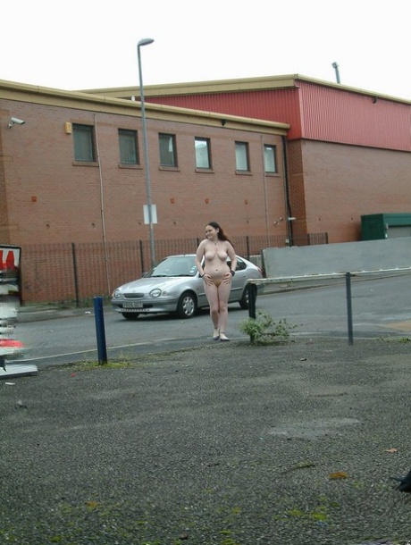 At a car park in an industrial area, the girl goes for her walk naked.