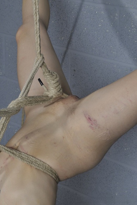 While unclothed, a woman with short hair is draped upside down by ropes.