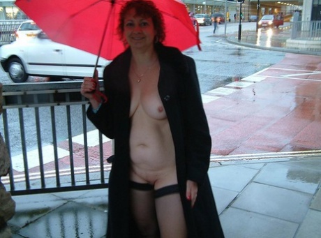 A British woman of middle age is naked in public while holding an umbrella.