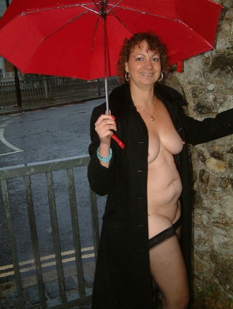 Wearing an umbrella, the elderly British lady participates in a nude public appearance while holding it.