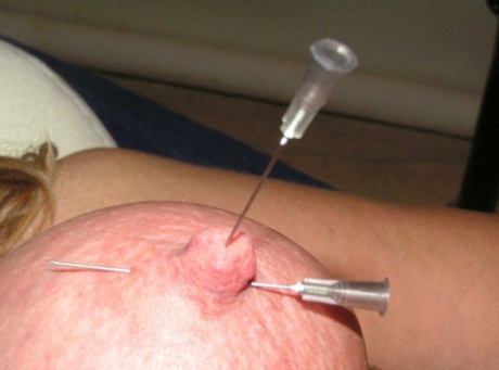 A blonde woman has her breasts and nipples pinched with needles.