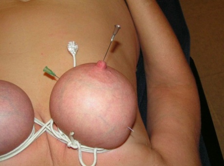 A woman who is blonde has her breasts and nipples pinched with needles.