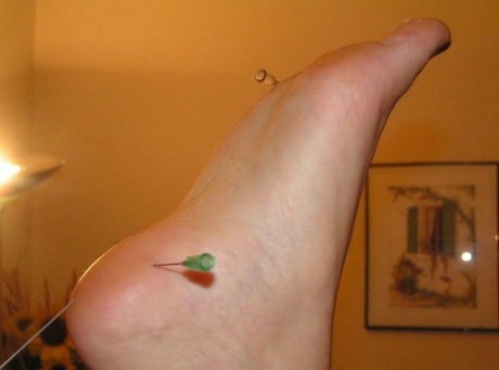 Needles are inserted into different body parts of a white girl who is restrained.