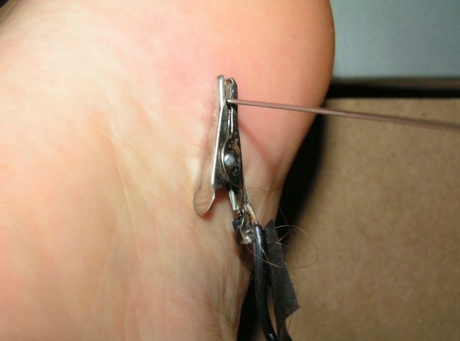 The needles are inserted into different body parts of a white girl who is restrained.