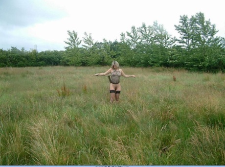 A bottomless blonde is attached to a bar that is connected to an electric fence.