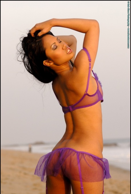 Asia Mckenzie, a seductive Asian woman, removes her transparent bra while lounging on the beach.