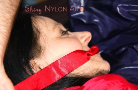 Wearing sexy red shiny nylon shorts and a bright orange shirt, Lucy tied and gagged on the bed with her hands tied.