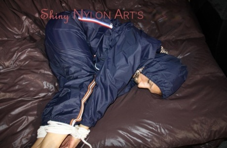 In a sensual attire, Sandra is dressed in shiny nylon rainwear and tied up with her hands.