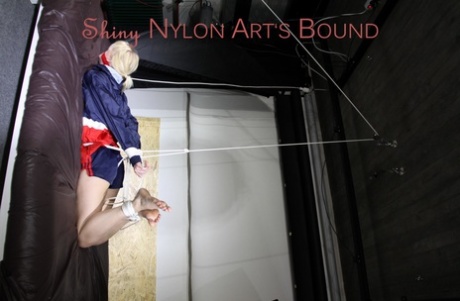 A blonde girl is seen wearing a nylon coat and shorts with her hands tied up and cleaved.