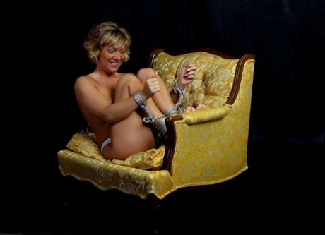 A topless blonde named MILF is tied down on a chair and secured in place with rope.