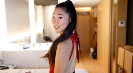 A woman of Asian descent in a black miniskirt undresses before engaging in POV sexual intercourse on a bed.