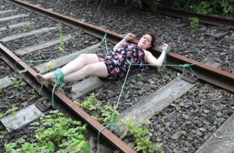 The train tracks are anchored to the head of a natural redhead while wearing a dress and glasses.