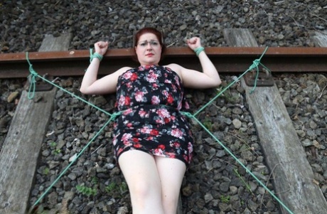 Dressed in glasses, the natural redhead is tied to train tracks.