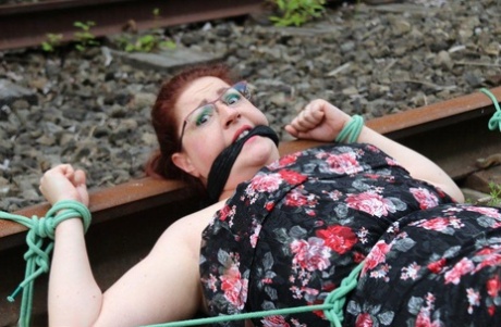 Dressed in clothing and glasses, a natural redhead is tied to train tracks.