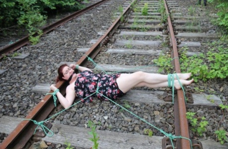 The train tracks are anchored to the head of a natural redhead while wearing a dress and glasses.