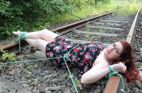 Dressed in glasses, the natural redhead is tied to train tracks.