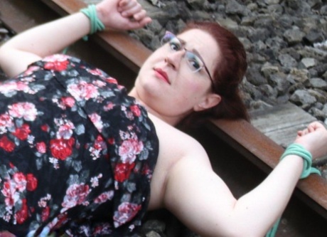 Dressed in glasses, the natural redhead is tied to train tracks.