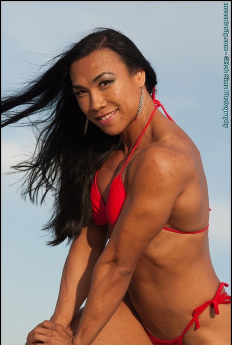In her red bikini on a beach, Asian fitness model Tram Nguyen displays her muscles.