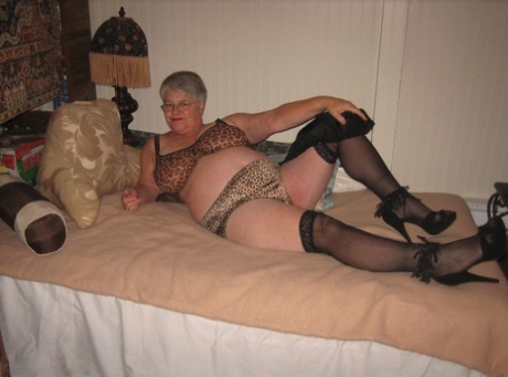 Masticating on her bed, the granny Girdle Goddess with silver hair and stockings bares her breasts.