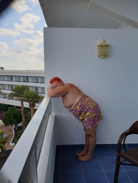 Obese nan sporting streaky red hair exposes her pants on the balcony and then poses in the nude.