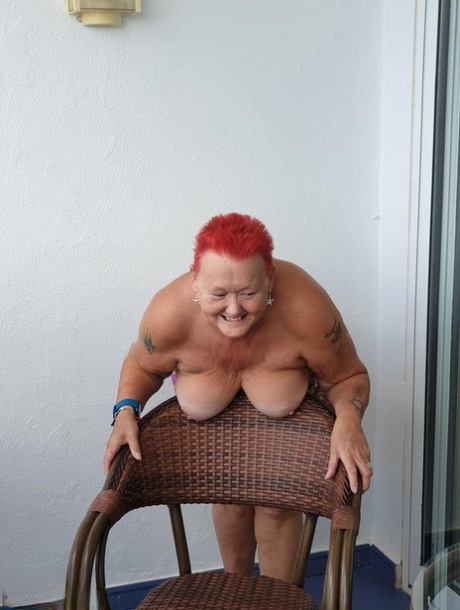 The unclothed nan with spiky red hair exposes her pants on the balcony and then poses for a photo in the nude.