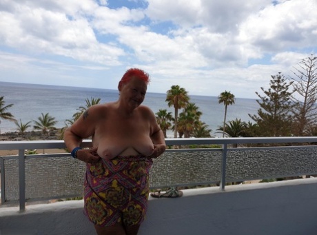 A naked nan with long hair and freckles exposes her pants on the balcony before posing for a picture, complete with flashy red lips.