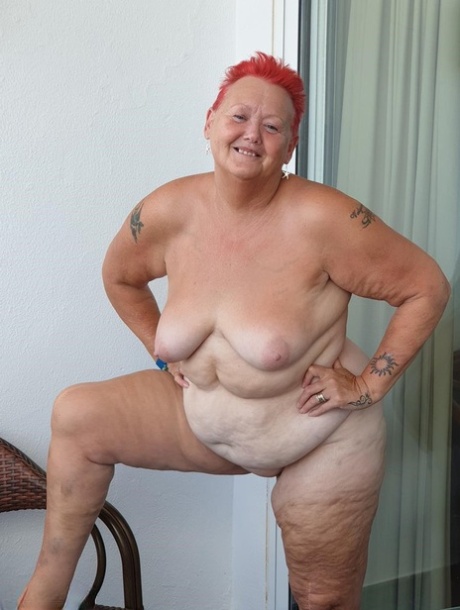 The overweight woman with red hair exposes her pants on the balcony before posing in an unclothed state.