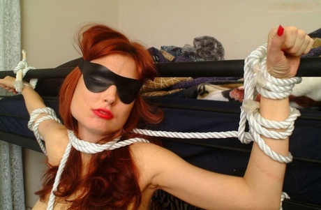 Red lips and a blindfold are worn by the naked redhead, who is tied up to a bunk bed.