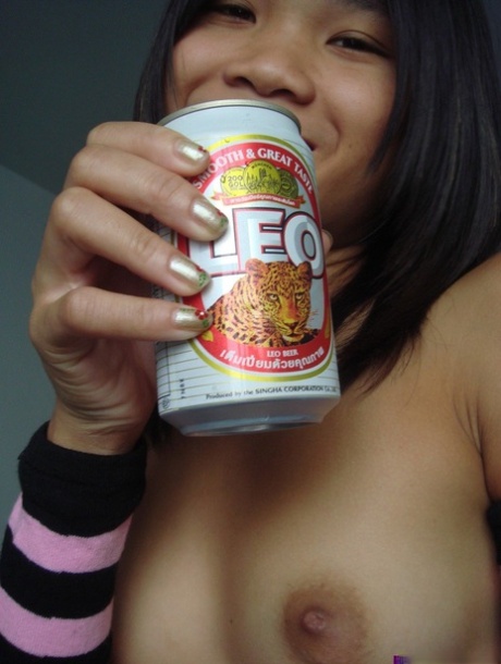 A little Asian female sips beer while pulling off armied socks and leggings.