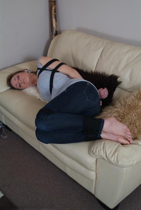 A girl dressed in clothing struggles on a loveseat, her legs tied in two places, and her stomach open.