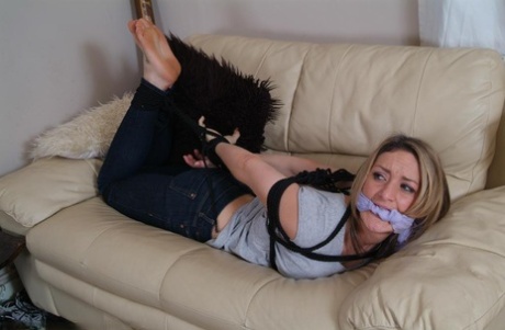 Dressed girl wrestles on a loveseat with her cleave fastened tightly and tied in the back.