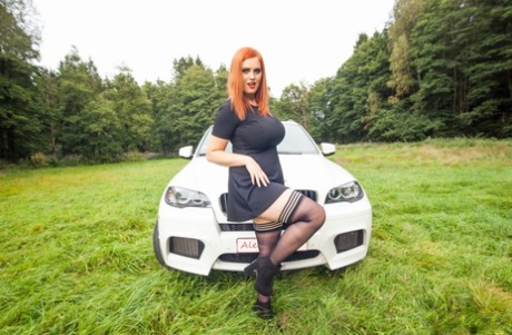 Redhead plumper Alexsis Faye loosens her giant tits on a car in the middle of a field.