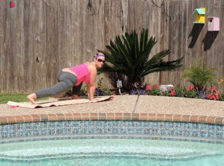 Dee Siren, who is overweight and has a blonde body, displays her prominent buttocks while practicing yoga near a swimming pool.