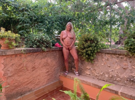 A young, blonde woman named Sweet Susi exits the garden without clothes by taking off a pink bra and panty before going naked.